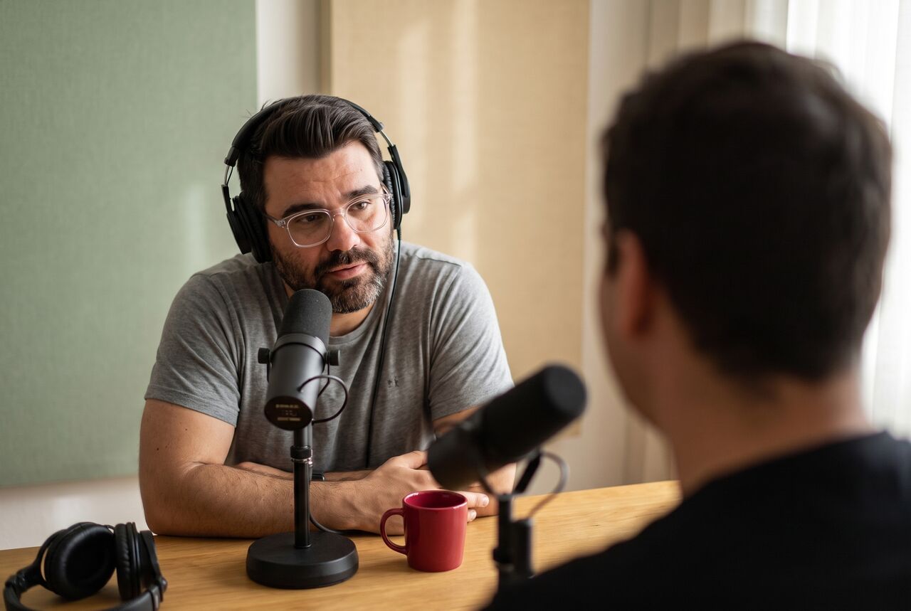 AI-generated photo of Richard in headphones at a podcast microphone, listening closely to a friend seen from behind